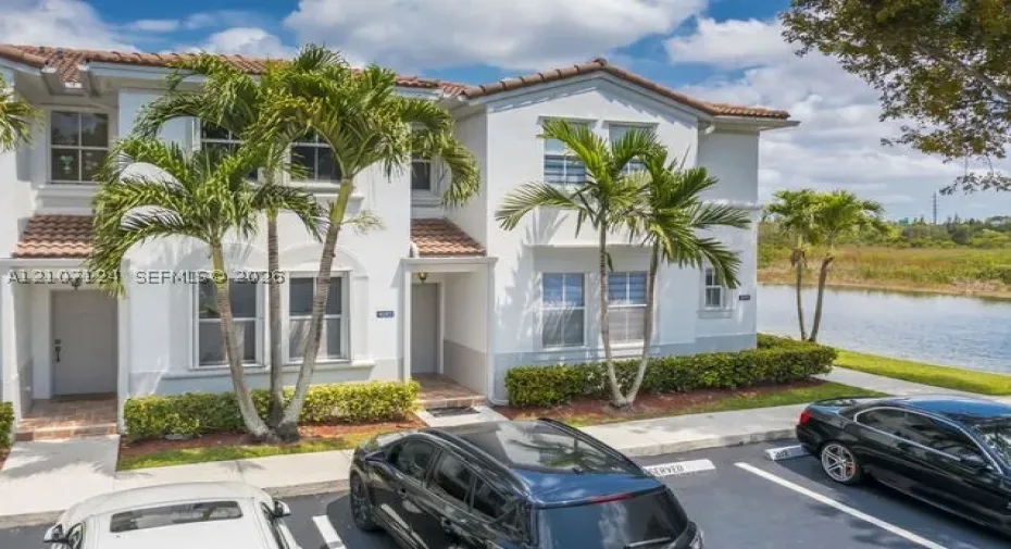 Two-story exterior featuring white stucco facade, tile roof, multi-pane windows, and a water-front setting