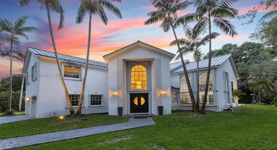 Stucco exterior featuring a metal roof, arched windows, grand double-door entrance, and a paved walkway