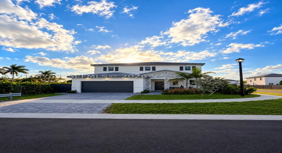 Two-story exterior featuring light-toned stucco finish, decorative stone accents, dark-toned concrete tile roofing, and a paved driveway