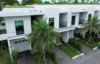 Modern architectural exterior featuring white stucco facade, second-story balconies with horizontal railing, private garages, and integrated rooftop landscaping