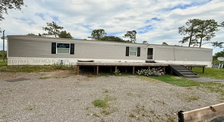 Single-story exterior with light gray horizontal siding, black shutter accents, and a raised wooden deck with integrated steps