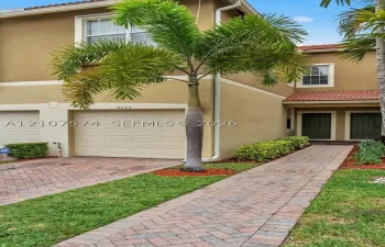 Two-story exterior featuring a stucco finish, tiled roof, attached garage, and a herringbone-patterned brick paver walkway