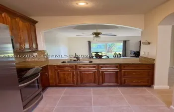 Kitchen featuring medium-toned wood cabinetry, stone countertops, stainless steel appliances, recessed ceiling lighting, and tile flooring