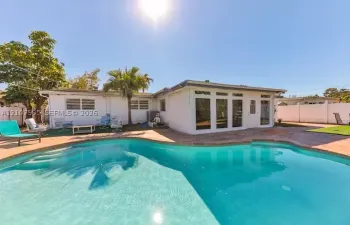 In-ground pool with stone paver surround, expansive patio space, white exterior siding, and custom glass-panel entry door
