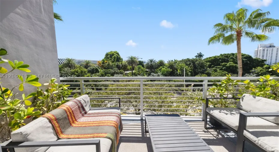 Private balcony featuring horizontal metal railing and mature tropical greenery