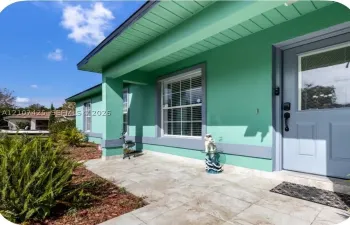 Covered front entryway featuring large-format tile flooring, a solid-core front door with an integrated glass pane, and multi-pane windows with contrasting trim
