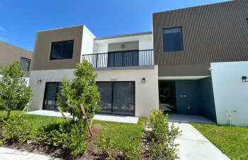 Contemporary exterior featuring corrugated metal siding, smooth stucco finish, a second-story balcony with black metal railing, and expansive glass sliding doors