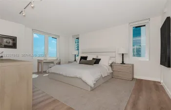 Room featuring wood-finish flooring, three windows with exterior urban scenery, and adjustable track lighting