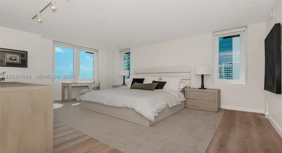 Room featuring wood-finish flooring, three windows with exterior urban scenery, and adjustable track lighting