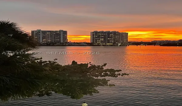 Waterfront setting featuring a prominent sunset backdrop, mature palms, and wide-water expanse