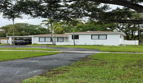 Single-story exterior featuring white masonry walls, a tile roof, an attached carport, and window frames with black trim