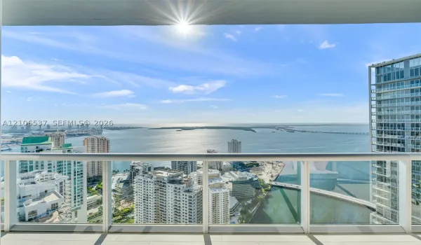Covered balcony with a glass-panel railing, tile flooring, and expansive water and urban skyline backdrop