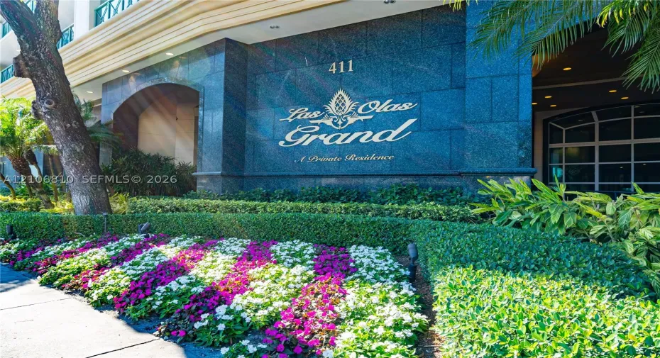 Polished stone facade featuring architectural signage, arched entryway, and manicured landscaping with formal garden beds