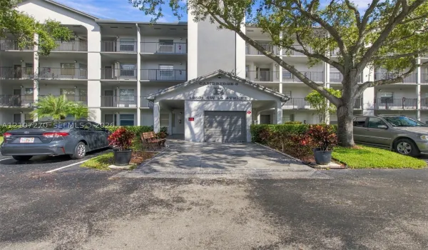 Multi-story exterior featuring a covered entryway, private garage, tiered balconies with metal railings, and mature landscaping