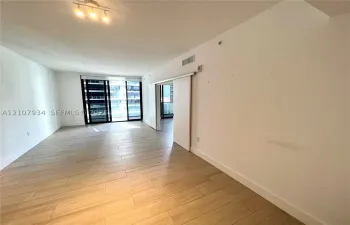 Open-concept living space featuring wood-finish flooring, sliding interior door, and floor-to-ceiling glass panel windows