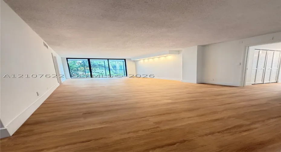 Open-concept room featuring wood-finish flooring, floor-to-ceiling sliding glass doors, built-in recessed soffit lighting, and closet doors with louvered panels
