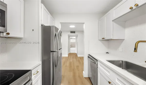 Kitchen featuring white Shaker-style cabinetry, light-toned composite countertops, stainless steel appliances, and wood-finish flooring