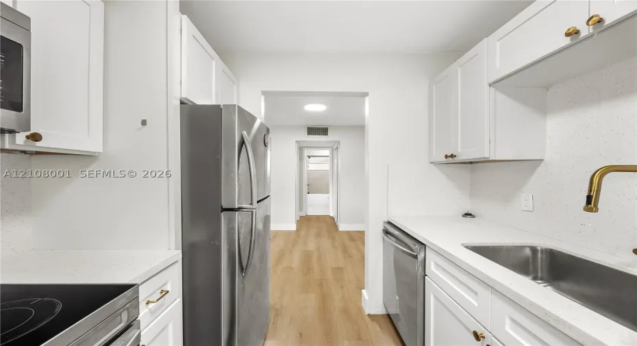 Kitchen featuring white Shaker-style cabinetry, light-toned composite countertops, stainless steel appliances, and wood-finish flooring