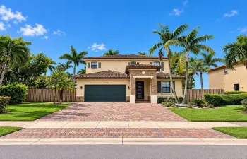 Two-story residence featuring a tile roof, decorative stone veneer accents, multi-pane glass entry door, and a paver driveway leading to an attached two-car garage