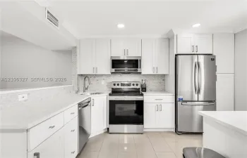 Kitchen featuring white shaker-style cabinetry, stainless steel appliances, quartz countertops, mosaic tile backsplash, and ceramic tile flooring