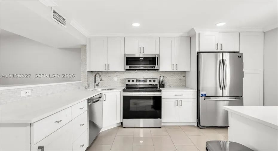 Kitchen featuring white shaker-style cabinetry, stainless steel appliances, quartz countertops, mosaic tile backsplash, and ceramic tile flooring