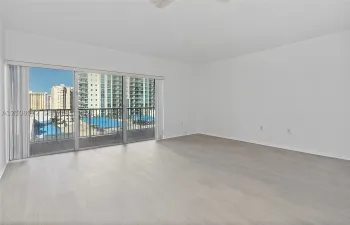Open-concept interior featuring light wood-finish flooring, sliding glass balcony doors, and a metal-railed balcony