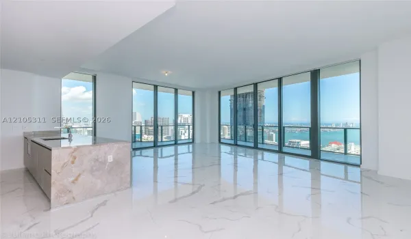 Expansive floor-to-ceiling windows, large format marble-look tile flooring, and a kitchen island with a stone countertop and integrated sink