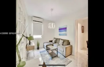 Living area featuring light-toned tile flooring, recessed ceiling lighting, a wall-mounted climate control unit, and French doors