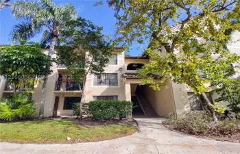 Multi-story exterior featuring a stucco facade, clay tile roof accents, private second-story balconies with iron railings, and concrete walkways