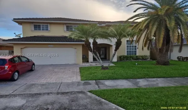 Two-story exterior featuring a tile roof, stucco finish, arched entryway, brick-paver driveway, and mature palm trees