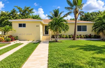 Manicured front lawn with mature palm trees, a concrete walkway, and a concrete driveway with grass strips