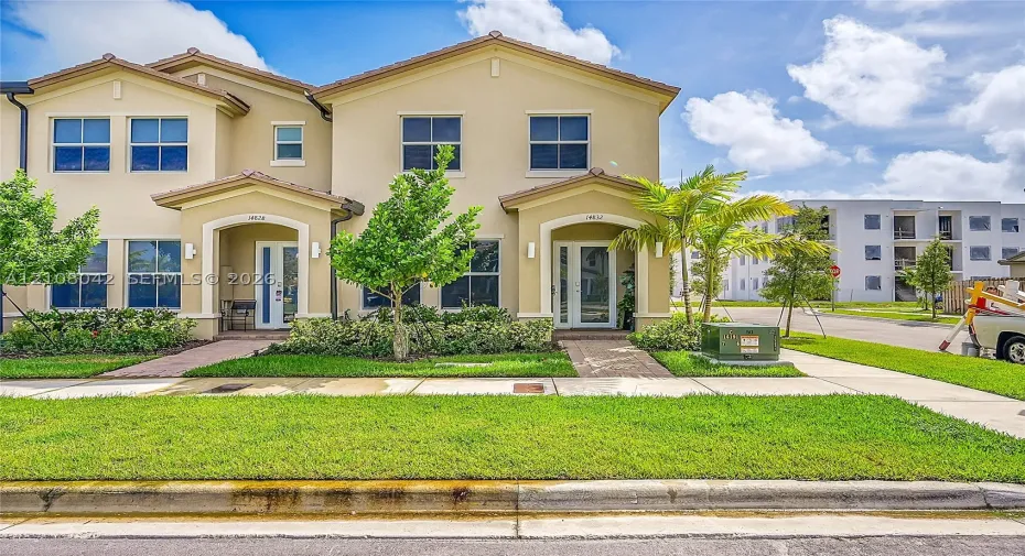 Two-story stucco exterior featuring a hipped roof, covered entryways with arched detailing, glass-panel front doors, and concrete walkways
