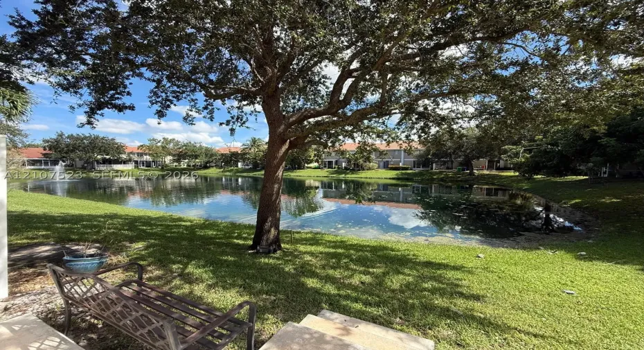 Waterfront lot featuring a natural pond, decorative fountain, mature shade trees, and manicured grass grounds