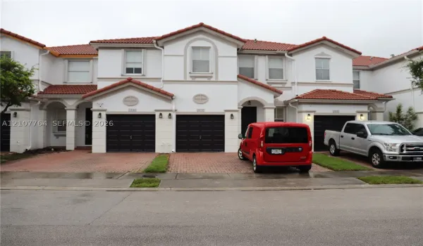 Mediterranean-inspired exterior featuring a multi-gabled tile roof, stucco facade, decorative arched detailing, and integrated multi-car garages with brick-paver driveways