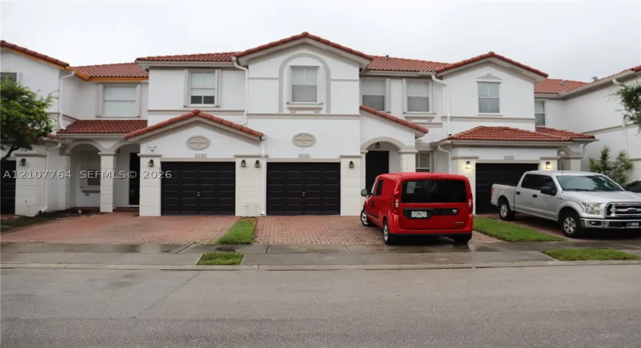 Mediterranean-inspired exterior featuring a multi-gabled tile roof, stucco facade, decorative arched detailing, and integrated multi-car garages with brick-paver driveways