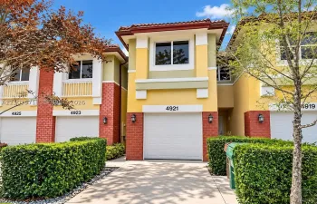 Multi-story townhouse exterior featuring a concrete driveway, integrated single-car garage, brick facade accents, and clay tile roofing