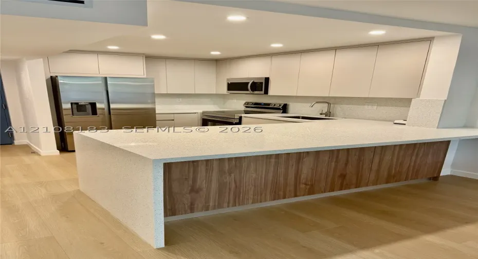Kitchen featuring flat-panel cabinetry, light-toned stone-finish countertops, wood-finish island paneling, recessed lighting, and stainless steel appliances