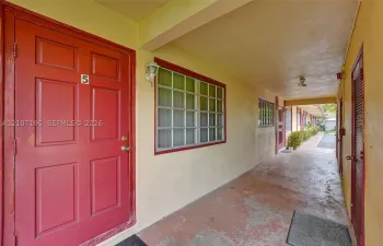 Covered exterior walkway featuring a concrete floor, multi-pane windows, and wall-mounted carriage-style lighting