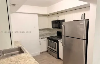 Kitchen featuring white cabinetry with matte black hardware, stone-patterned countertops, stainless steel appliances, a tile backsplash, and wood-finish flooring