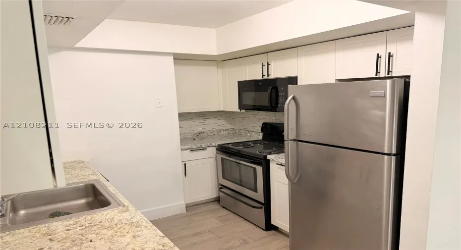 Kitchen featuring white cabinetry with matte black hardware, stone-patterned countertops, stainless steel appliances, a tile backsplash, and wood-finish flooring