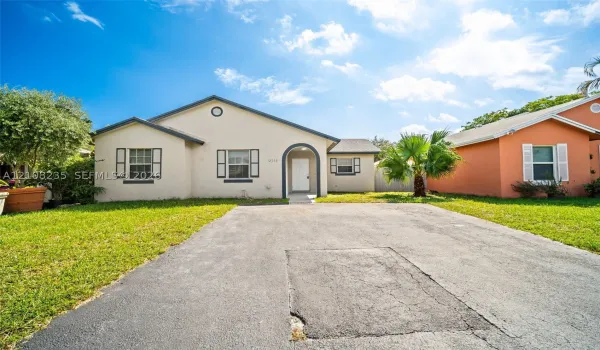 Single-story stucco exterior featuring an arched entryway, decorative shutters, and an asphalt driveway