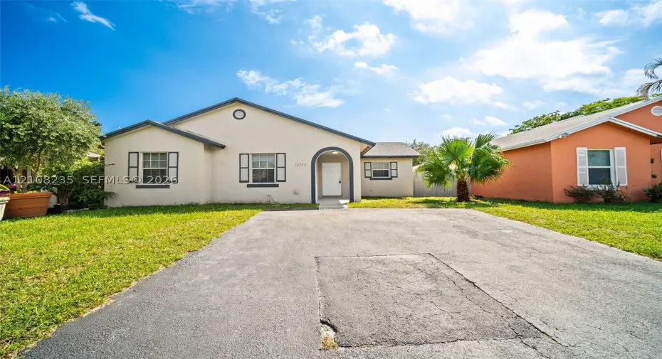Single-story stucco exterior featuring an arched entryway, decorative shutters, and an asphalt driveway