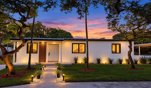 Single-story residence featuring a smooth stucco exterior, dark-trimmed windows, a metal roof, and a vertical wood-slat accent wall at the entryway, complemented by a landscaped front yard with a concrete walkway