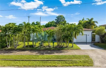 Single-story residence featuring a low-slope roof, attached one-car garage, concrete driveway, and established tropical landscaping