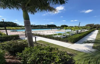 Swimming pool with concrete decking, surrounding black metal fencing, synthetic turf accents, and perimeter landscaping