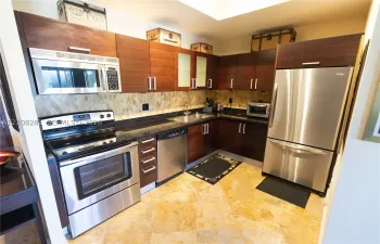 Kitchen featuring dark wood-finish cabinetry, stainless steel appliances, stone-finish countertops, geometric-pattern backsplash tile, and stone-finish flooring
