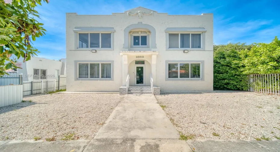 Two-story building exterior featuring a textured stucco facade, decorative architectural molding, window awnings, and a covered entryway