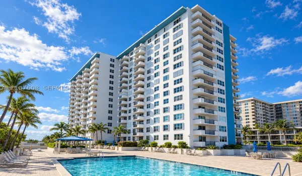 High-rise residential exterior featuring stacked private balconies, ground-level swimming pool, paved pool deck, and mature palm trees