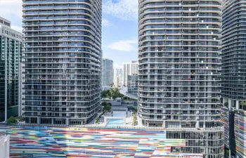 High-rise residential towers featuring wrap-around glass balconies, exterior multi-colored mural facade, and outdoor swimming pool