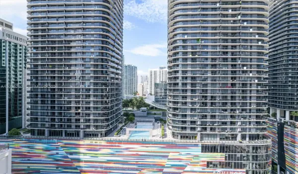 High-rise residential towers featuring wrap-around glass balconies, exterior multi-colored mural facade, and outdoor swimming pool